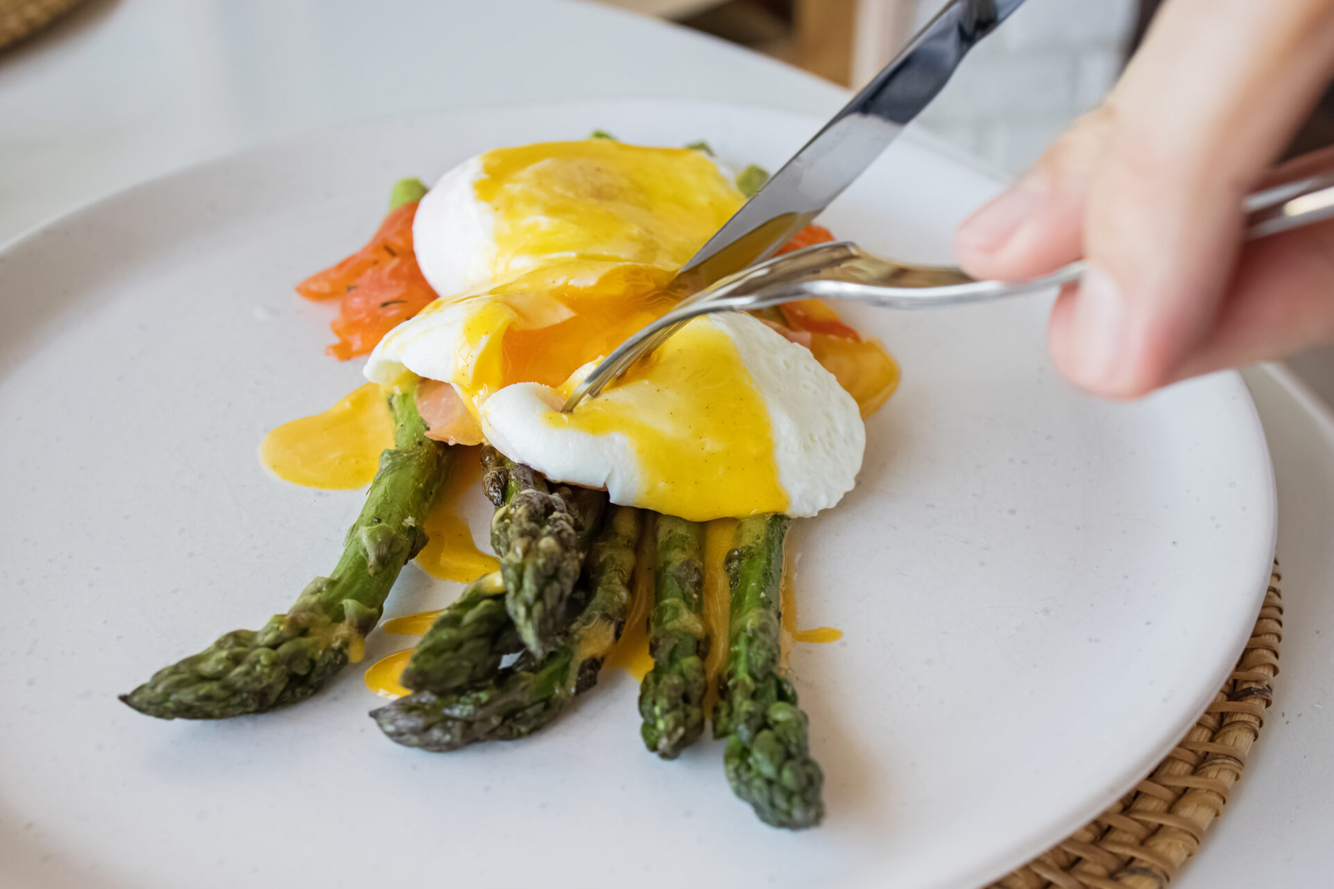 Man's hands cutting poached egg with hollandaise sauce and salmon over asparagus