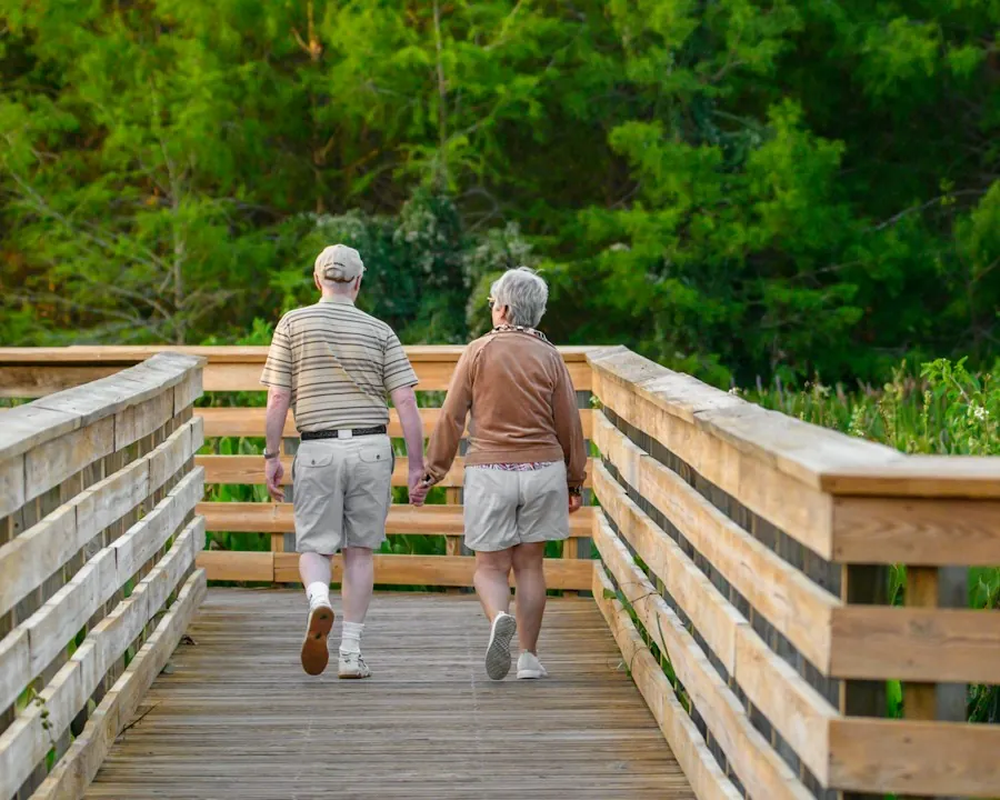 Pareja mayor paseando por una pasarela de madera entre árboles