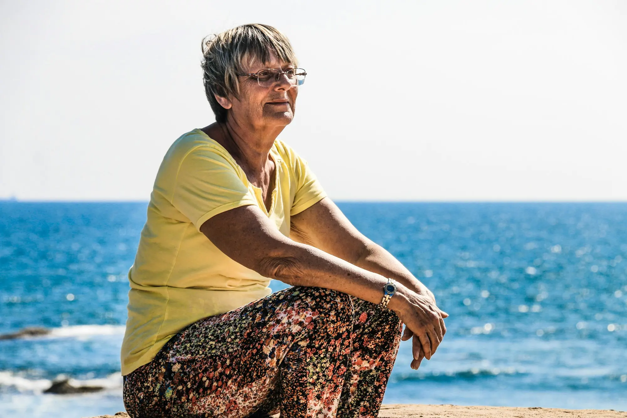 Mujer mayor sentada en las rocas frente al mar, al sol