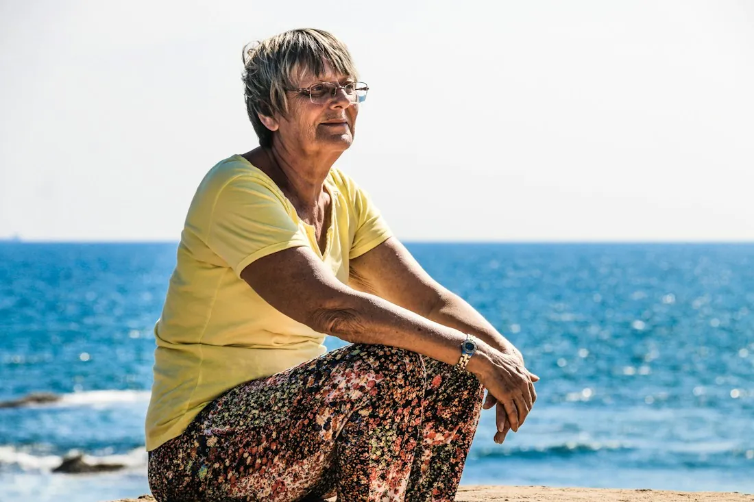 Mujer mayor sentada en las rocas frente al mar, al sol