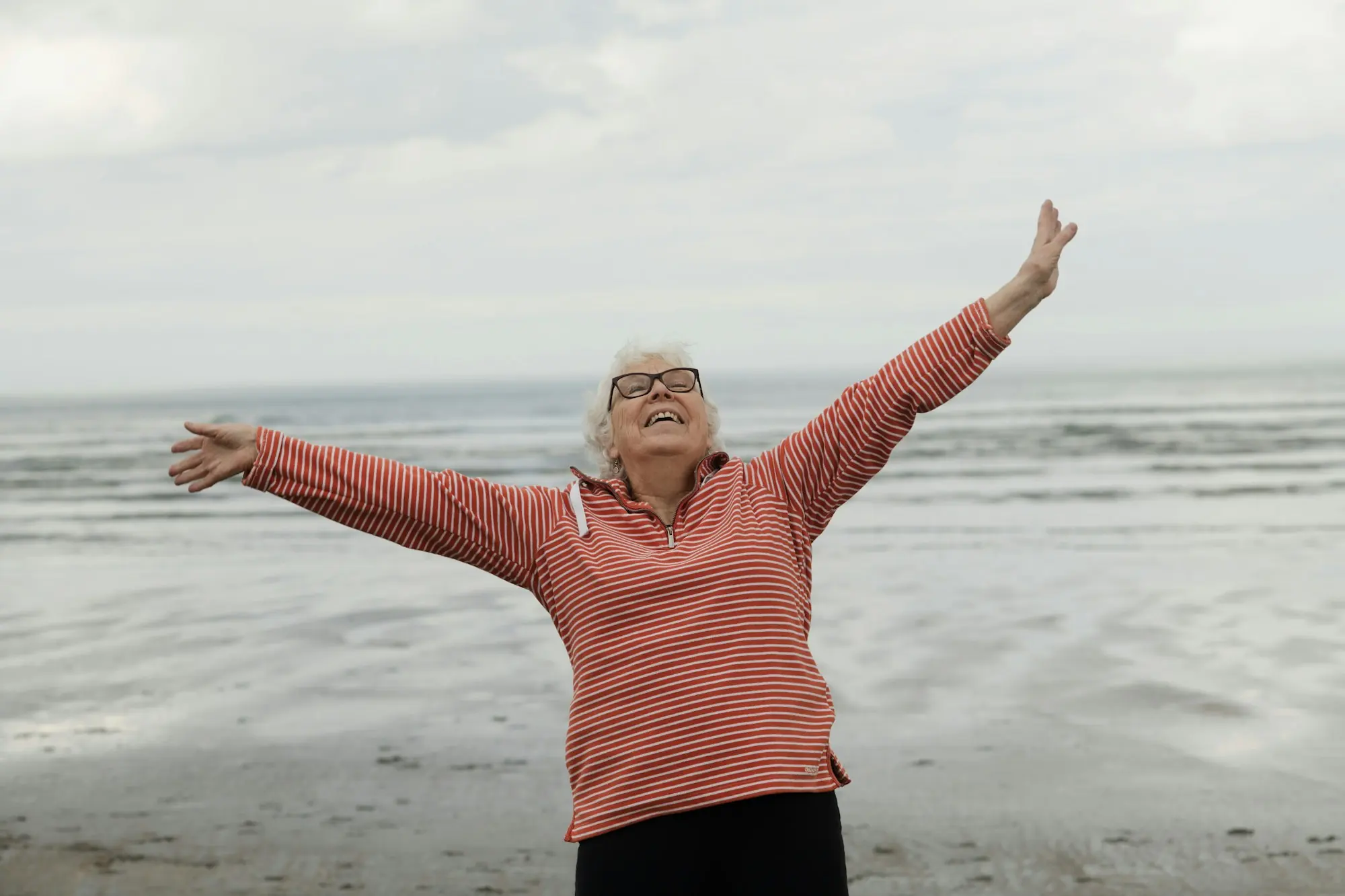 Mujer mayor con los brazos abiertos en la orilla del mar