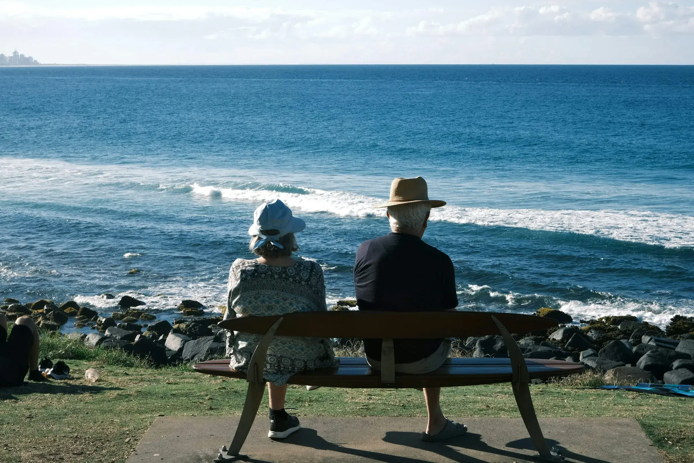 Pareja mayor con sombrero, sentada en un banco frente al mar