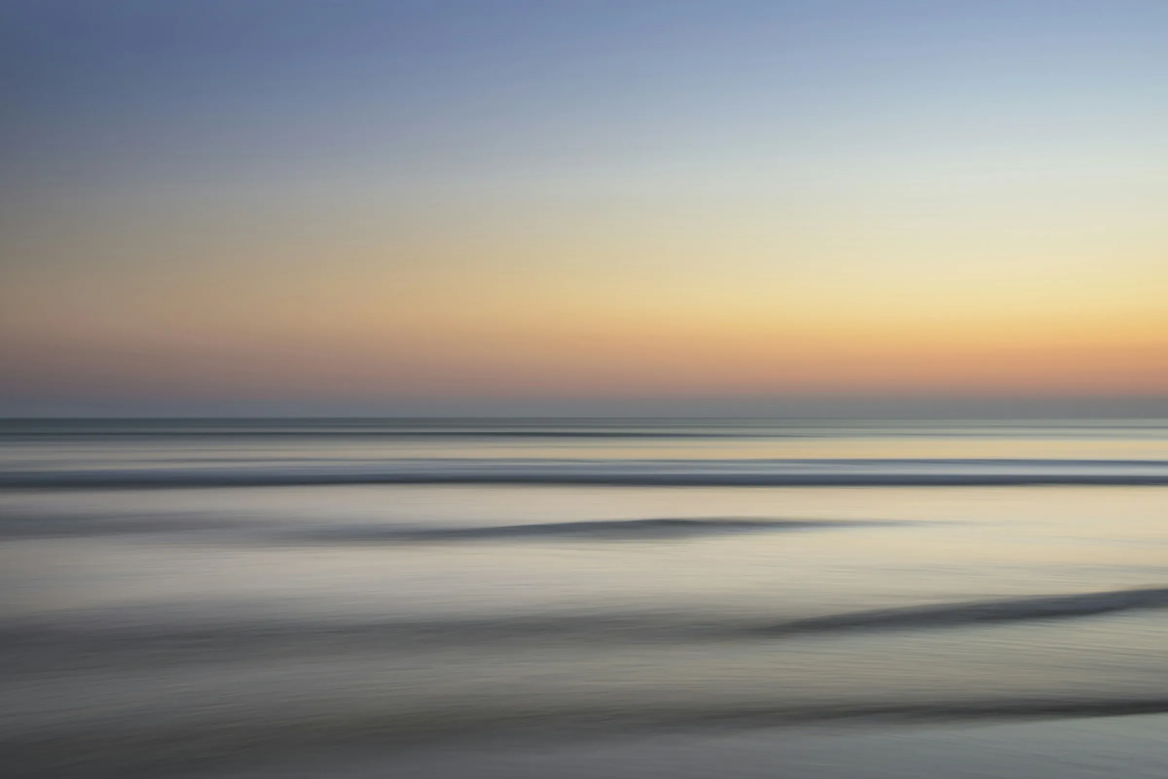 Mar en calma al amanecer, con el horizonte en tonos naranja y azul